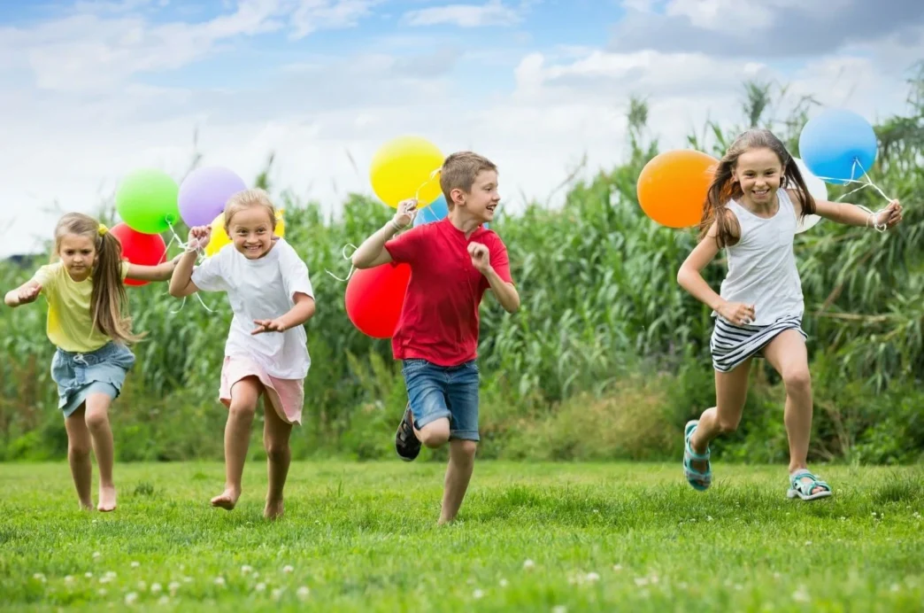 Día del Niño: Niños felices corren en el parque con globos de colores. Celebración familiar en un espacio abierto. Actividades para niños.