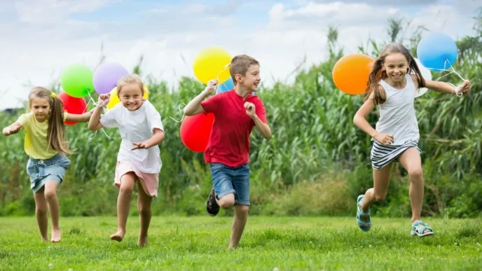 Día del Niño: Niños felices corren en el parque con globos de colores. Celebración familiar en un espacio abierto. Actividades para niños.
