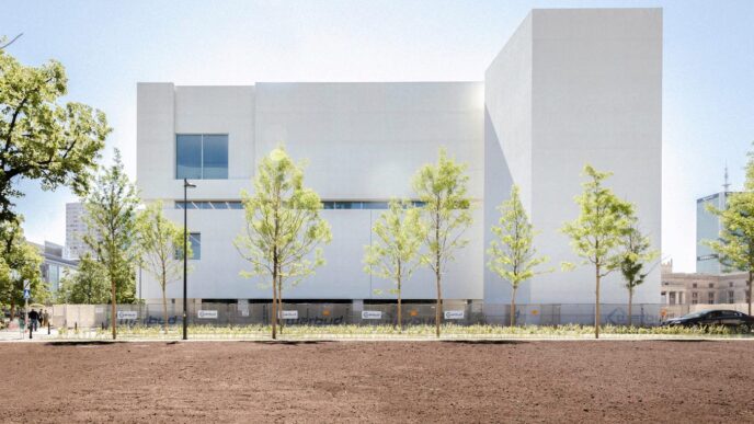 Vista exterior del Dovetail Building. Multiplex asegura contrato millonario. Fachada blanca, árboles jóvenes y explanada en primer plano. Diseño arquitectónico.