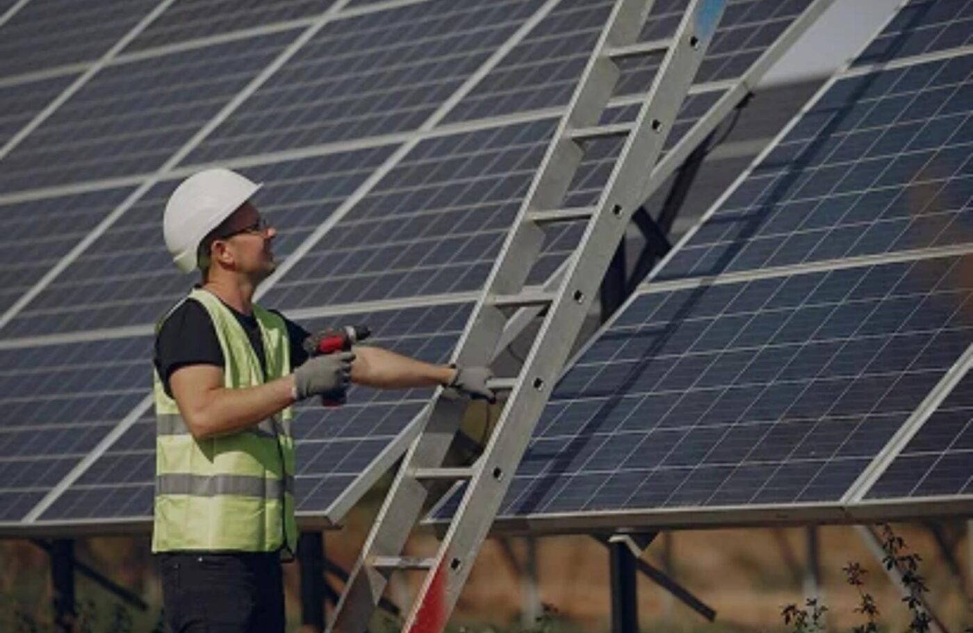 Instalador con casco ajustando paneles solares para construcción eficiente energéticamente. Escalera y herramientas visibles. NJBPU impulsa la energía solar.
