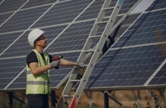 Instalador con casco ajustando paneles solares para construcción eficiente energéticamente. Escalera y herramientas visibles. NJBPU impulsa la energía solar.