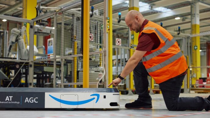 Trabajador de Amazon en nuevo centro logístico de Asturias interactúa con robot automatizado. Tecnología avanzada para operaciones eficientes.
