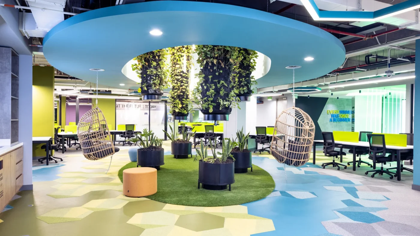 Diseño innovador de Oficinas AEI Spaces: Espacios abiertos con plantas colgantes, sillas colgantes de mimbre y mobiliario moderno y colorido.