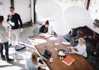 Grupo diverso trabaja flexible en oficina moderna con laptops. Espacio colaborativo y lámparas esféricas ofrecen ambiente inspirador y productivo.