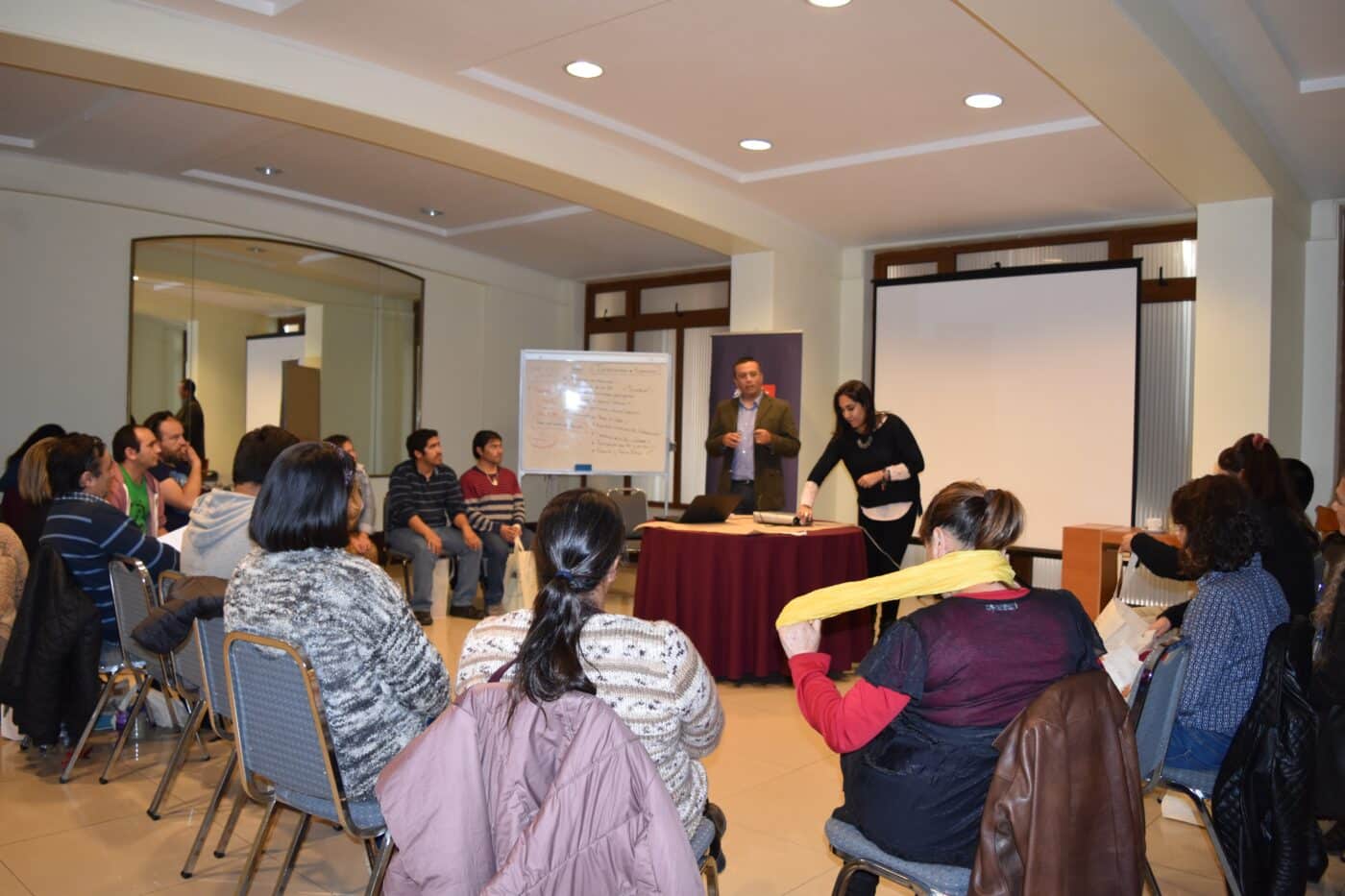 Venue/Architecture
Dos personas presentan en Inmobiliare Summits, frente a una audiencia sentada. Pizarra blanca y pantalla de proyección visibles. Conferencia.