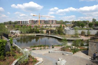 Vista panorámica de un parque urbano con un lago, puente peatonal, edificios residenciales y una grúa, resaltando el desarrollo de ciudades.