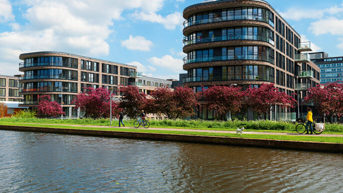 Edificios modernos holandeses junto al canal, árboles en flor. Inversión inmobiliaria en Holanda. Cielos azules. Perspectivas de inversión.
