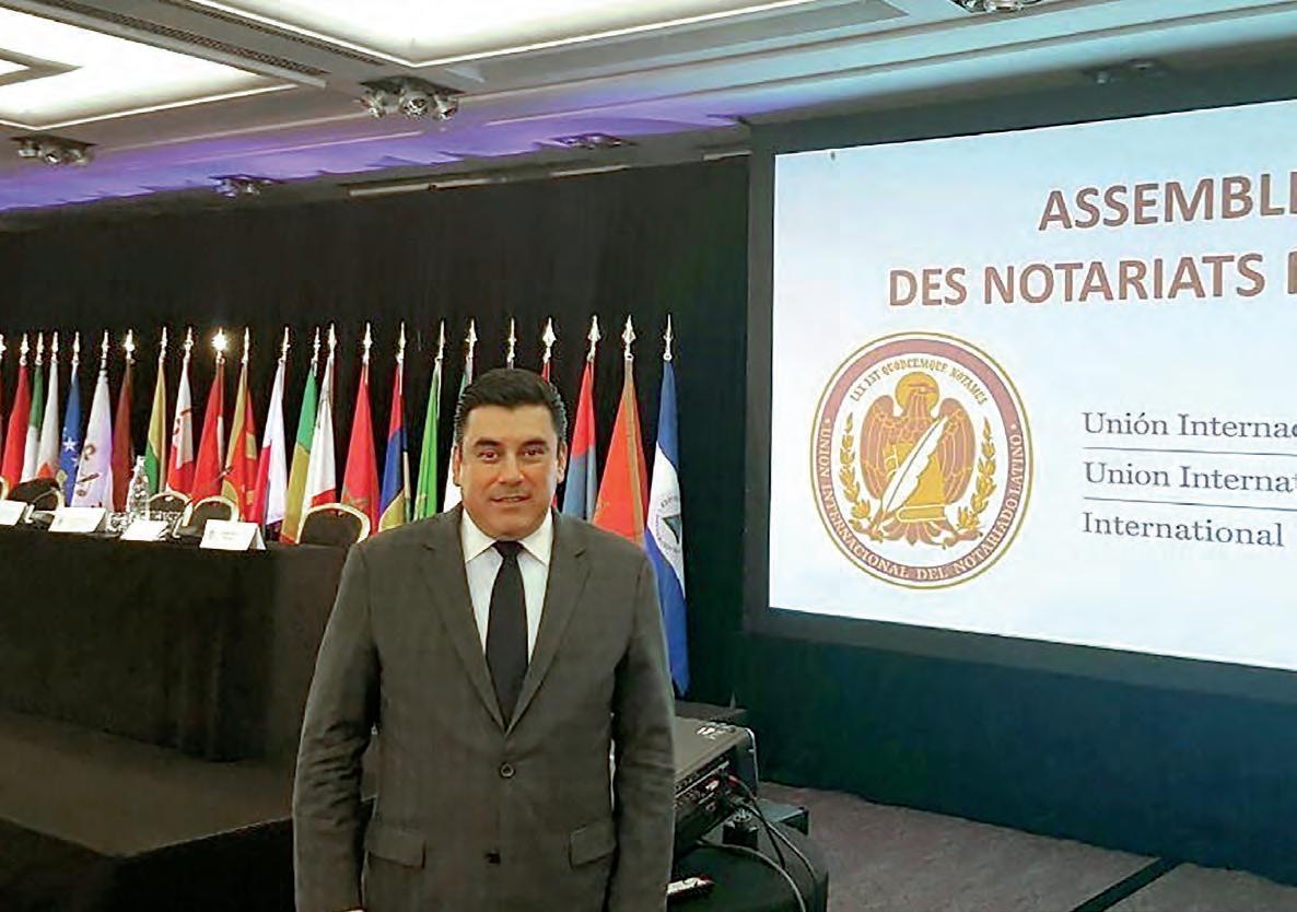 Speakers/headshot

Orador en evento LATAM. Un hombre sonríe frente a banderas y pantalla con texto en francés y español. Conferencia internacional.