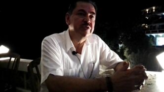 Hombre con camisa blanca, posible ganador Premio Cemex Sedatu, hablando. Fondo nocturno difuso. Reconocimiento Sedatu a obras destacadas 2023.