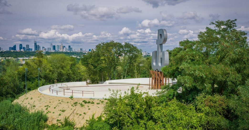 Escultura en parque con horizonte urbano, posible sede de Inmobiliare Summits. Espacio verde en ciudad, evento real estate LATAM.
