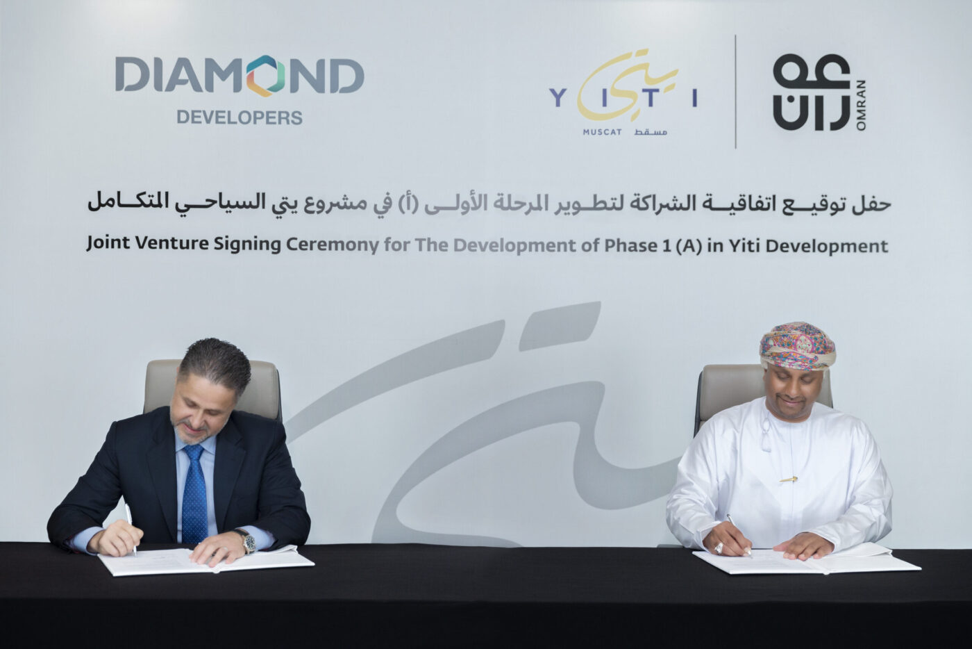 Ceremonia de inversión inmobiliaria turística en Yiti: dos hombres firman acuerdo. Logos de Diamond Developers, Yiti y Omran visibles.