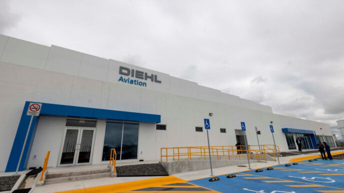 Vista exterior de la primera planta de Diehl Aviation en América, ubicada en Querétaro, con señalización y estacionamiento accesible. Edificio moderno y amplio.