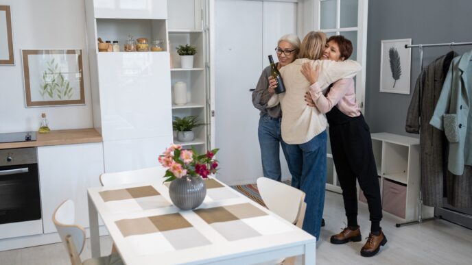 Dos mujeres abrazan a una tercera que llega con una botella de vino. Diseño de interiores, vivienda, bienes raíces, hogar.