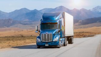 Camión azul en carretera con montañas al fondo, clave en nearshoring. Logística eficiente para Puerto Cancún, impulsando el crecimiento económico regional con 124