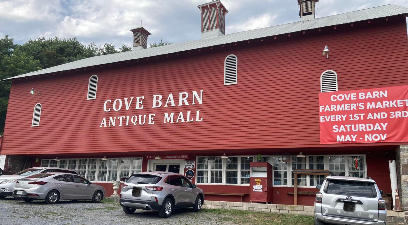 Vista del Cove Barn Antique Mall, una estructura roja grande con un banner anunciando el mercado de agricultores los sábados 1° y 3° de cada mes.