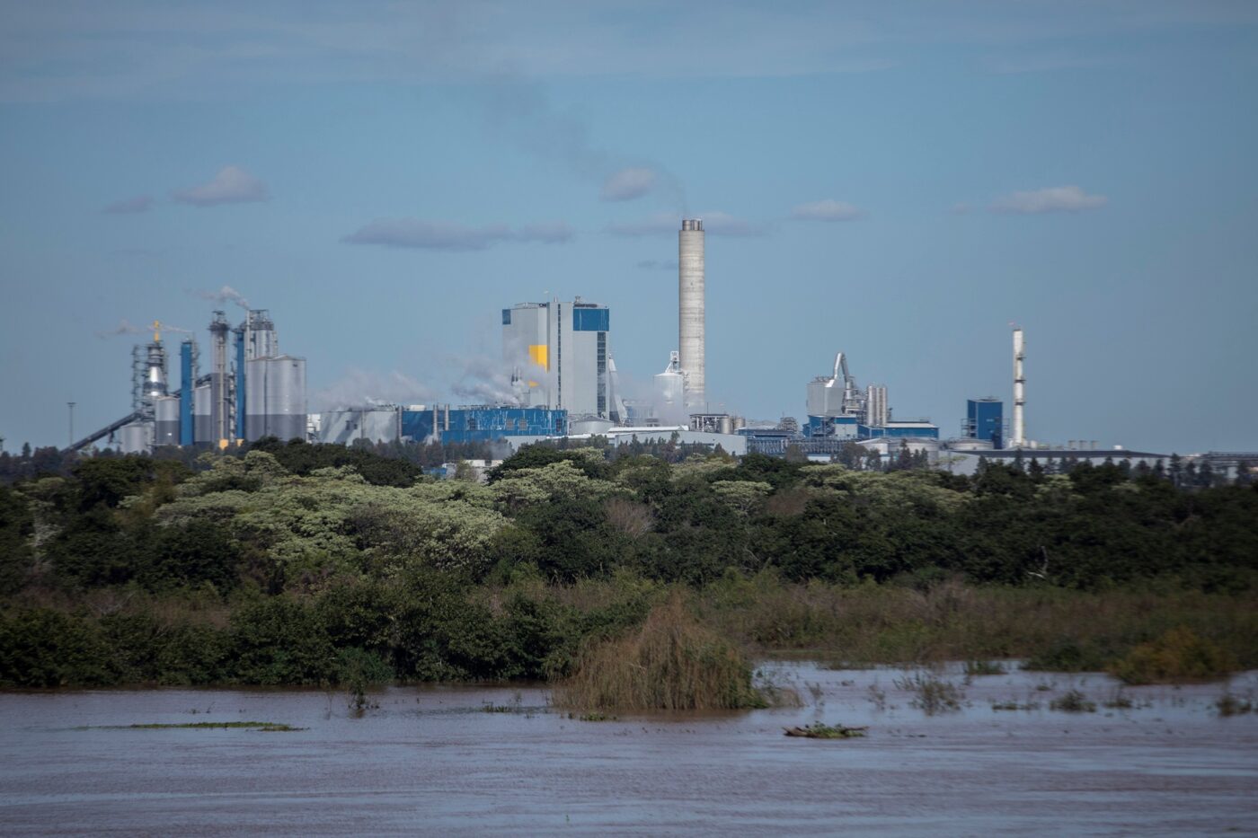 Vista del Molino Giot, Uruguay, un complejo industrial con chimeneas y edificios junto al río, reflejando el proyecto inmobiliario de recuperación.