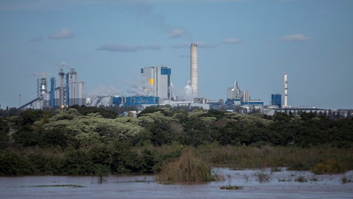 Vista del Molino Giot, Uruguay, un complejo industrial con chimeneas y edificios junto al río, reflejando el proyecto inmobiliario de recuperación.