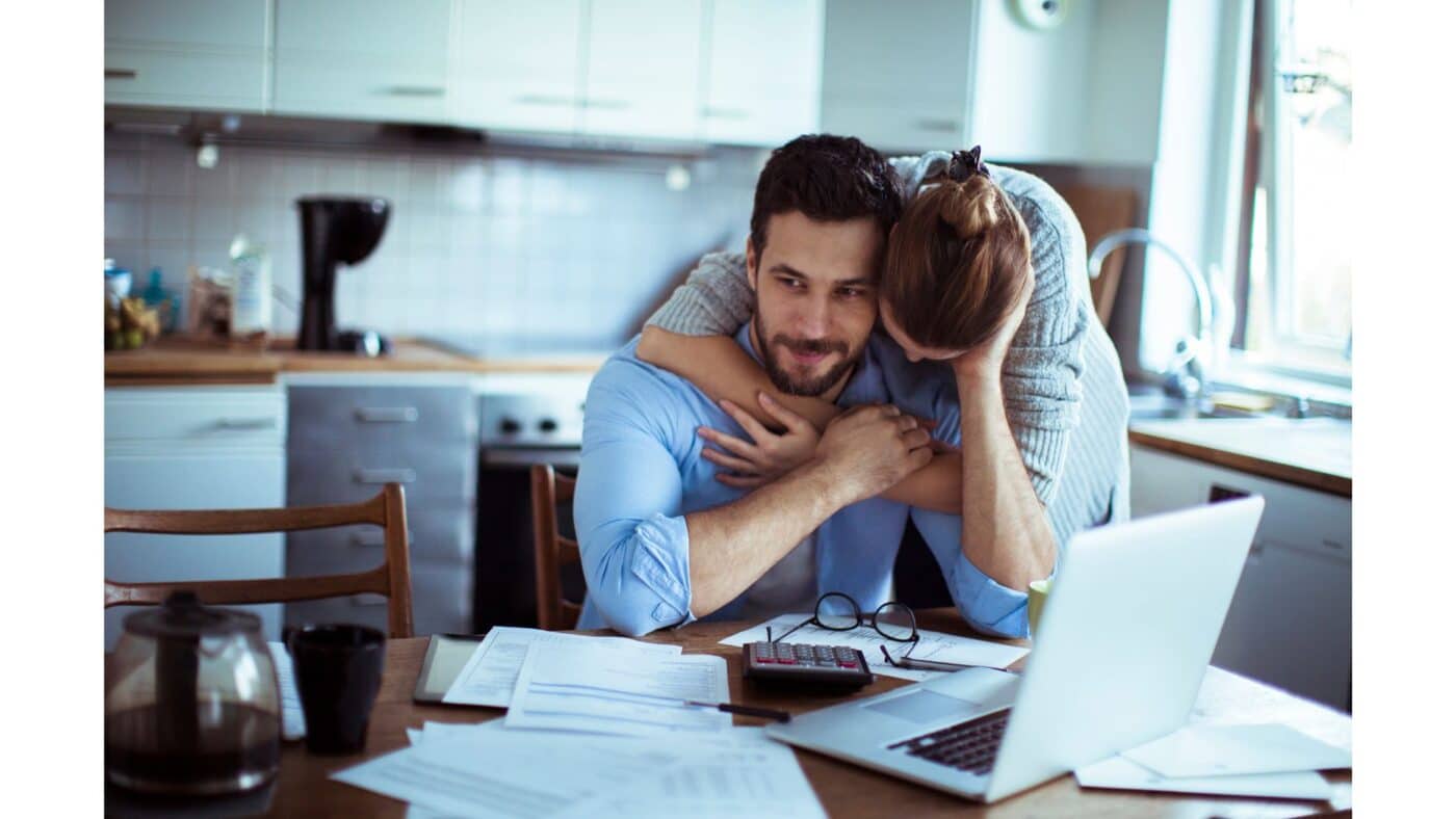 Pareja joven revisando gastos para rentar con roomies; una opción viable para compartir gastos y ahorrar. Hombre con laptop y mujer abrazándolo.