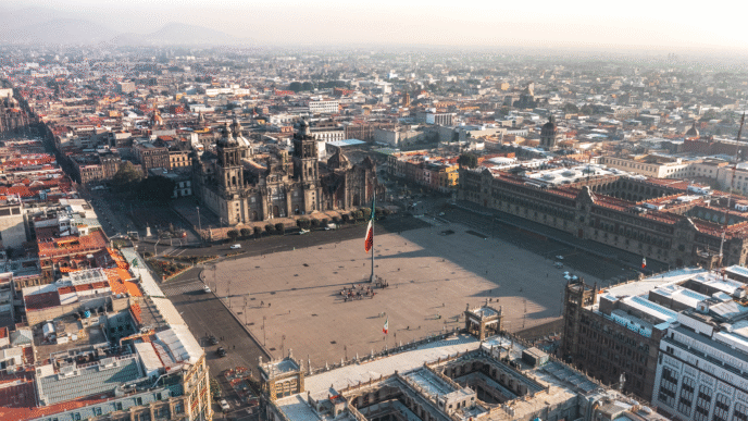 Vista aérea del Zócalo en CDMX. Impacto en inversionistas inmobiliarios por aumento en rentas. Catedral Metropolitana y Bandera de México.
