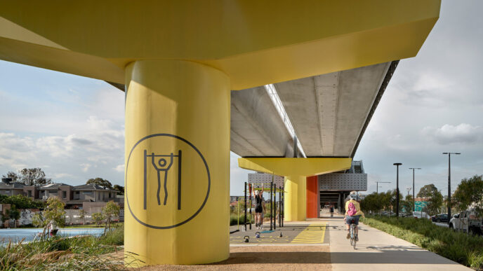 Espacio urbano revitalizado con área de calistenia bajo puente amarillo. Ciclista y persona haciendo ejercicio. Participación comunitaria activa.