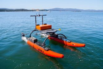 Barco autónomo Robosys WAM-V modernizado con IA navegando en el mar. Catamarán naranja equipado con sensores para operaciones autónomas e inteligentes.