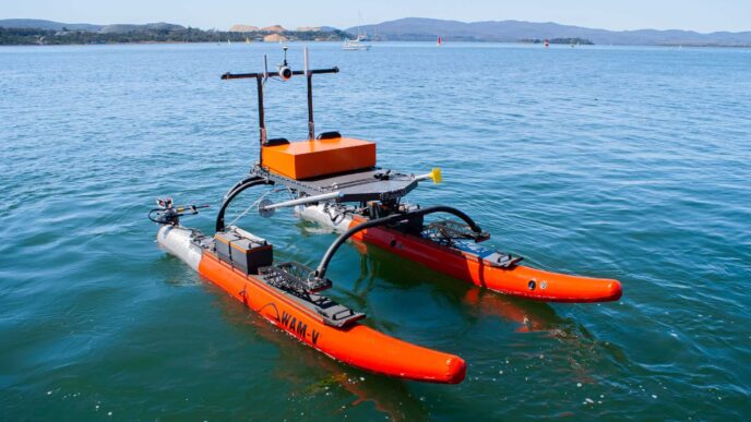 Barco autónomo Robosys WAM-V modernizado con IA navegando en el mar. Catamarán naranja equipado con sensores para operaciones autónomas e inteligentes.