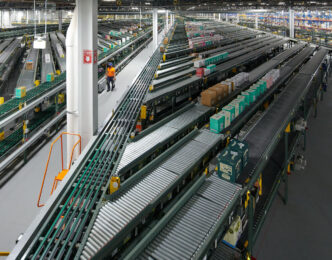 Visión amplia de un almacén con cintas transportadoras y operario. Automatización y tecnología transformando el real estate industrial.