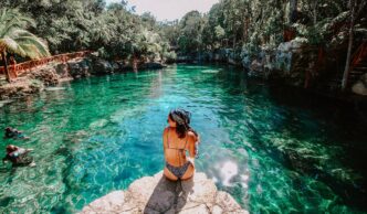Turismo de salud en México: Mujer contempla la belleza natural de un cenote con aguas cristalinas. El paraíso perfecto para relajación y bienestar.