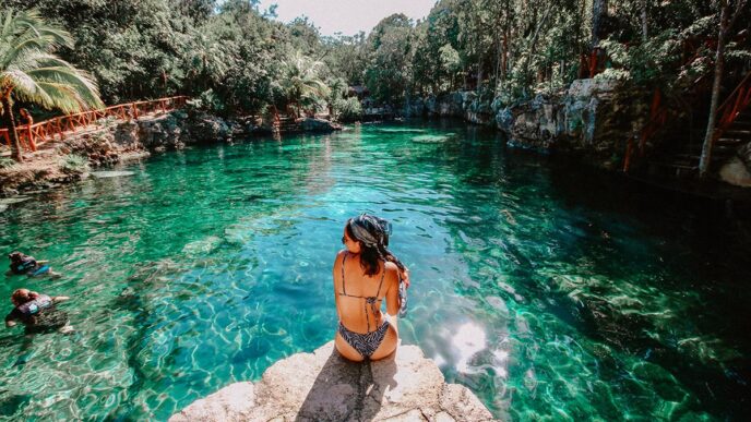 Turismo de salud en México: Mujer contempla la belleza natural de un cenote con aguas cristalinas. El paraíso perfecto para relajación y bienestar.