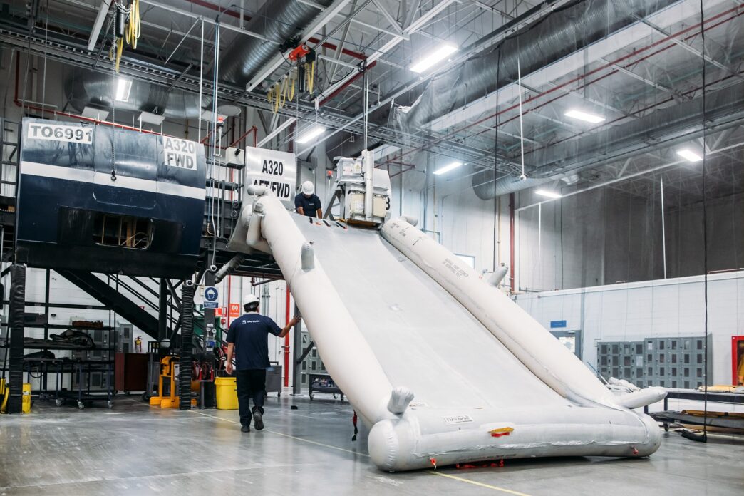 Venue/architecture.
Dos trabajadores inspeccionan un tobogán de emergencia de un avión A320 en un hangar industrial. Mantenimiento aeronáutico.