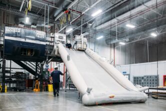 Venue/architecture.
Dos trabajadores inspeccionan un tobogán de emergencia de un avión A320 en un hangar industrial. Mantenimiento aeronáutico.