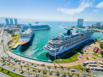 Vista aérea de cruceros en México, anticipando la llegada de seis millones de cruceristas. Terminal moderna con barcos imponentes y ciudad al fondo.
