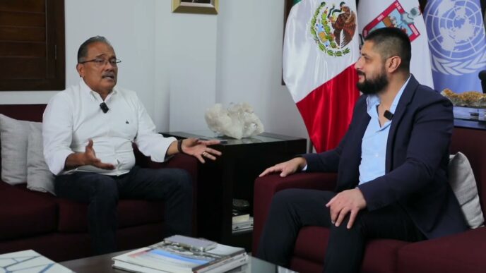 Reunión sobre inversión de Seojin Mobility en Nuevo León. Dos hombres en sillones con banderas de México y ONU de fondo, discutiendo detalles clave.