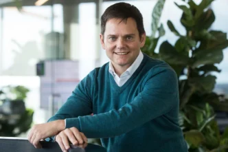 Retrato de un ejecutivo sonriendo, SL Green, impulsando el crecimiento en arrendamiento de oficinas. Fondo moderno con vegetación y luz natural.