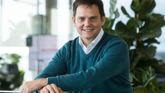 Retrato de un ejecutivo sonriendo, SL Green, impulsando el crecimiento en arrendamiento de oficinas. Fondo moderno con vegetación y luz natural.