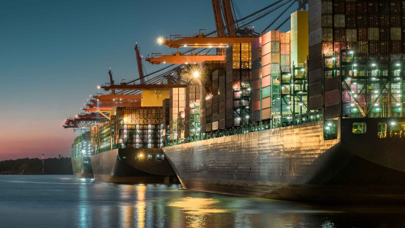 Vistas nocturnas de buques de carga en puerto mostrando logística marítima sostenible e impacto en el Real Estate, con grúas iluminadas.
