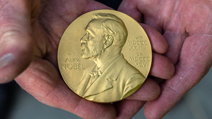 Primer plano de la medalla del Premio Nobel de la Paz, con el perfil de Alfred Nobel, sostenida en las manos. Subasta de la casa del Nobel.