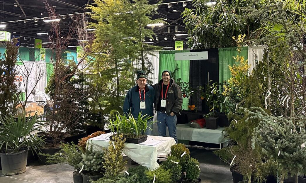 Networking/expo.

Exhibición de vivero en Inmobiliare Summits. Dos personas posan frente a su stand en la conferencia de real estate. Variedad de plantas y árboles en venta.