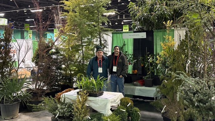 Networking/expo.

Exhibición de vivero en Inmobiliare Summits. Dos personas posan frente a su stand en la conferencia de real estate. Variedad de plantas y árboles en venta.