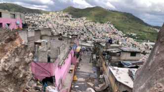 Vista panorámica de una ciudad en LATAM, con casas coloridas en una ladera. Arquitectura urbana y entorno natural contrastantes.