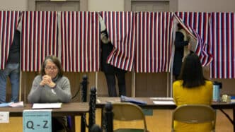 speakers/headshot
Personas votando en cabinas con cortinas de rayas rojas, blancas y azules. Elecciones en EE. UU. con votantes y mesas de registro.