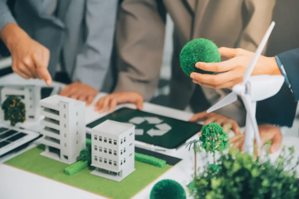Equipo inmobiliario planea transformación verde: modelos de edificios, turbina eólica y símbolo de reciclaje. Residuos en valor inmobiliario.