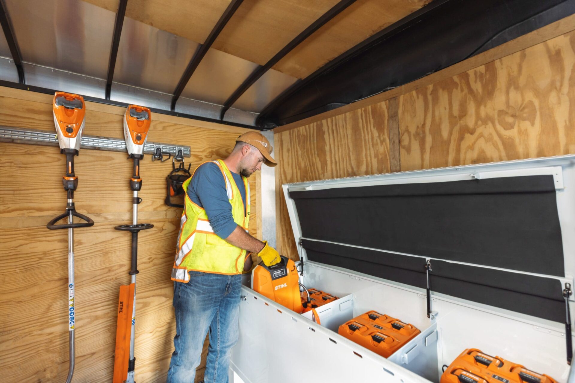 Hombre cargando baterías de litio Stihl en remolque con equipos eléctricos de jardinería. Transición a equipos eléctricos en paisajismo con baterías.
