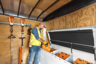 Hombre cargando baterías de litio Stihl en remolque con equipos eléctricos de jardinería. Transición a equipos eléctricos en paisajismo con baterías.