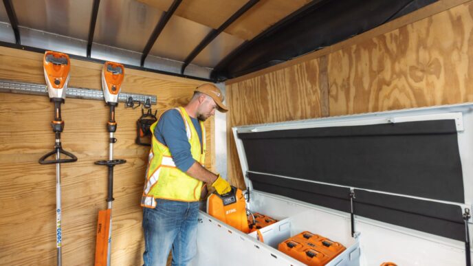 Hombre cargando baterías de litio Stihl en remolque con equipos eléctricos de jardinería. Transición a equipos eléctricos en paisajismo con baterías.