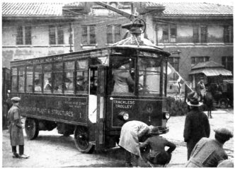 Antiguo tren interurbano en blanco y negro de Nueva York, con la leyenda 'Trackless Trolley' y personas alrededor. Transporte urbano de época.
