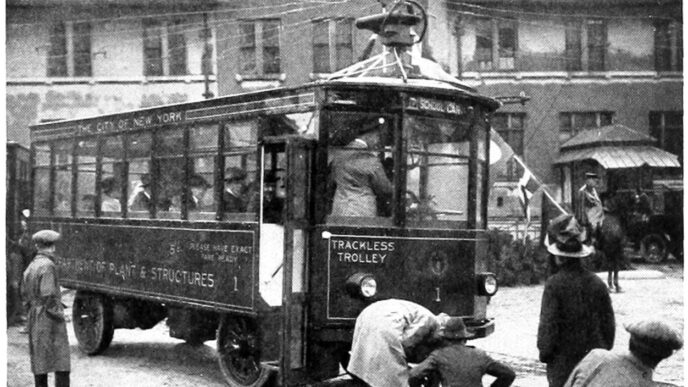 Antiguo tren interurbano en blanco y negro de Nueva York, con la leyenda 'Trackless Trolley' y personas alrededor. Transporte urbano de época.