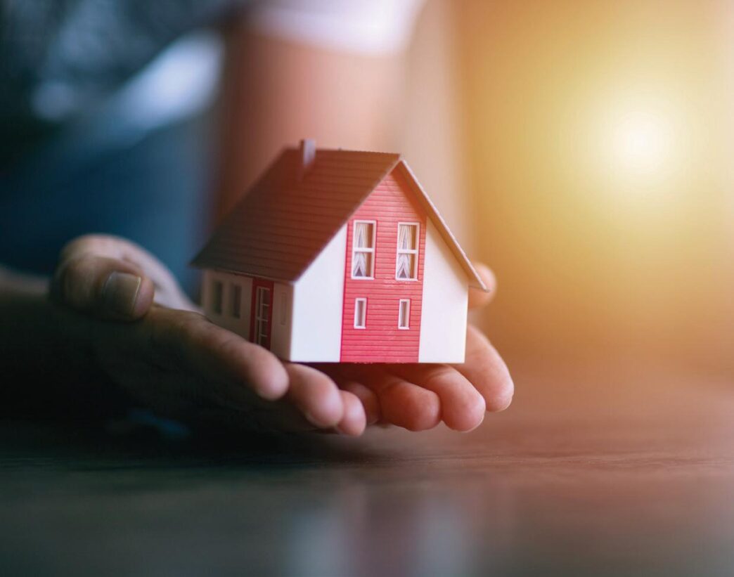 Abstracto: Mano sostiene una casa modelo. Impacto en venta de viviendas en Colombia. Inmobiliare Summits analiza el sector real estate.