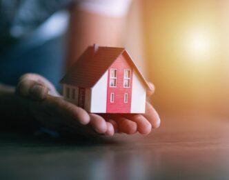 Abstracto: Mano sostiene una casa modelo. Impacto en venta de viviendas en Colombia. Inmobiliare Summits analiza el sector real estate.