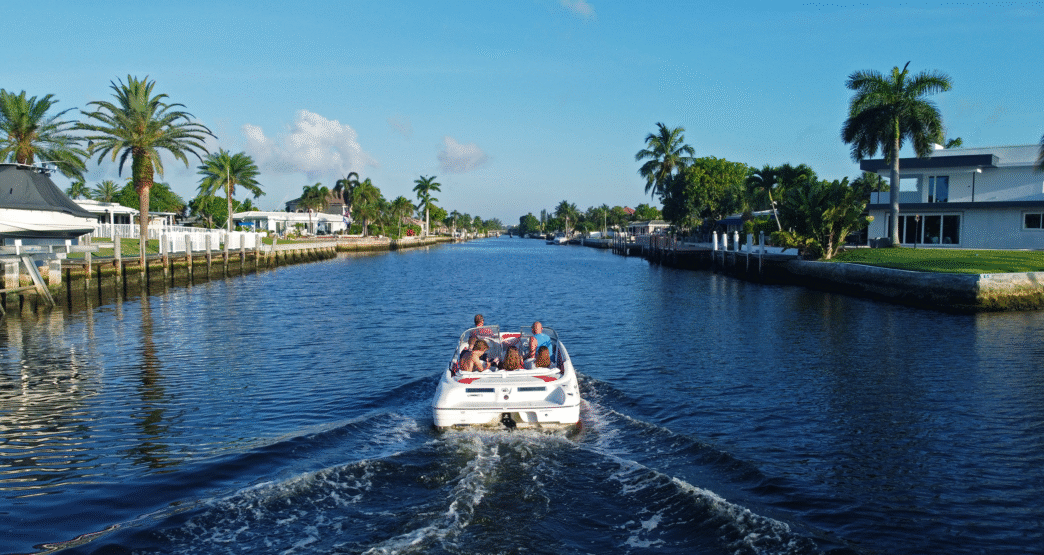 Ciudad turística soleada. Lancha navega por canal bordeado de palmeras y casas. Inversión inmobiliaria en destinos turísticos de México.